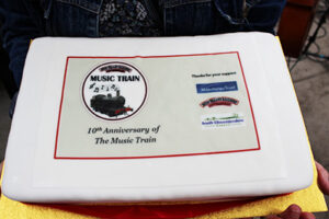 A photo of a cake. The cake has the words '10th anniversary of the Music Train' written in the icing sugar